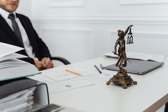 A professional lawyer in a suit sits at a desk with a Lady Justice statue. Trust our expertise as your Truck Accident Lawyer in San Antonio.