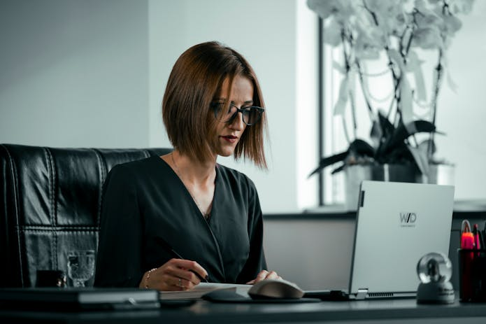 Female professional with glasses at desk using laptop, Dallas Truck Accident Injury Attorney.