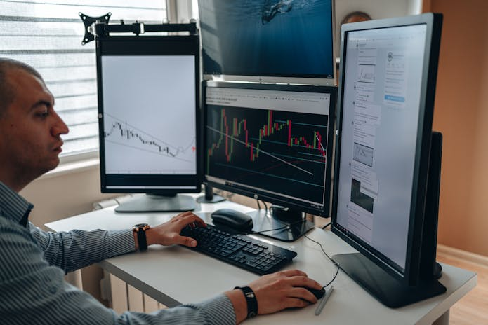  Picture of a man at a computer with several monitors, illustrating the best performance management systems for small enterprises.