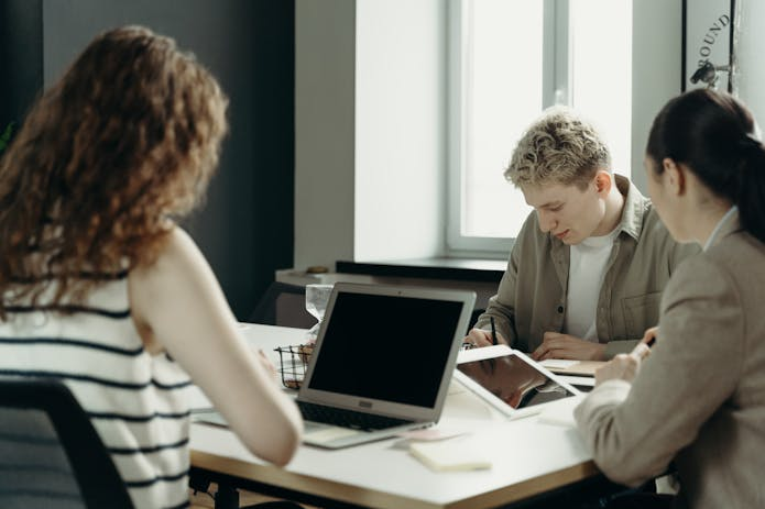 Three individuals seated at a table with laptops, using the Best Help desk App.