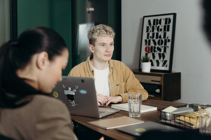 Get the Best Help Desk App! Boost productivity with our user-friendly software - a man at a table with a laptop and two women.