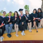 A group of graduates sitting on a wall, celebrating their achievement after earning the most affordable online master's degree in accounting.