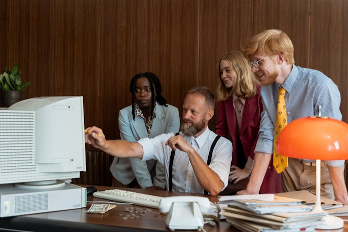 A diverse group of individuals gathered around a computer screen, engrossed in analyzing the best performance management systems for small companies.