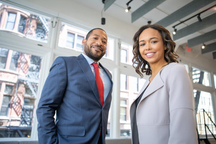 Corporate man and woman in business attire posing in front of window, embodying Houston 18 Wheeler Attorney.