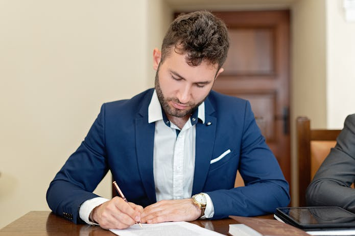 PIP attorneys near me: Two men in suits seated at a table, signing important documents.