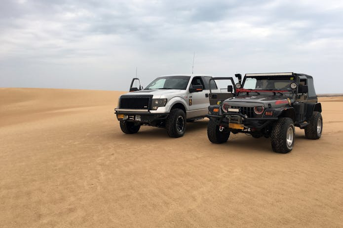 Experience the thrill of the desert with two jeeps parked in the sand dunes. Seek a truck accident injury law firm close by.