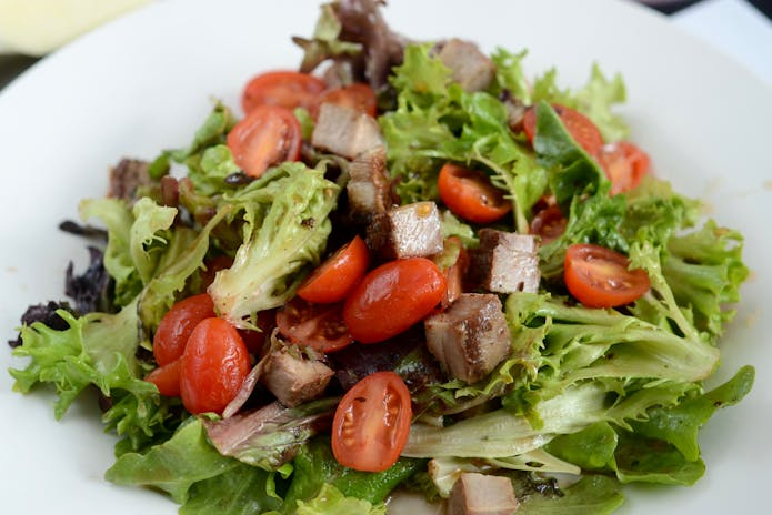 A delicious salad with meat, tomatoes, and lettuce on a white plate at Nish Nūsh chilis Restaurants in New York.