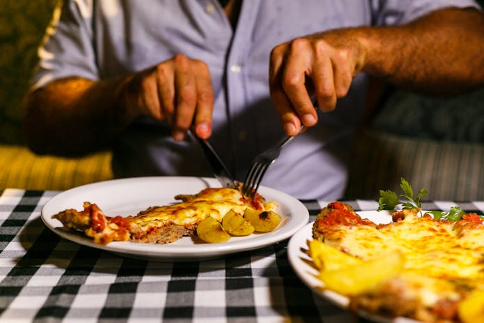 A man enjoying pizza with utensils at a popular fast food place in New York.