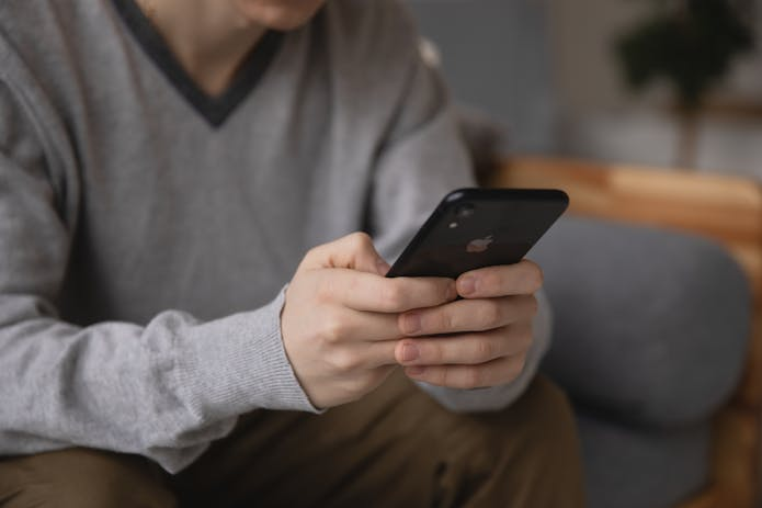  Man sitting on couch, using phone, unveiling iOS 18.