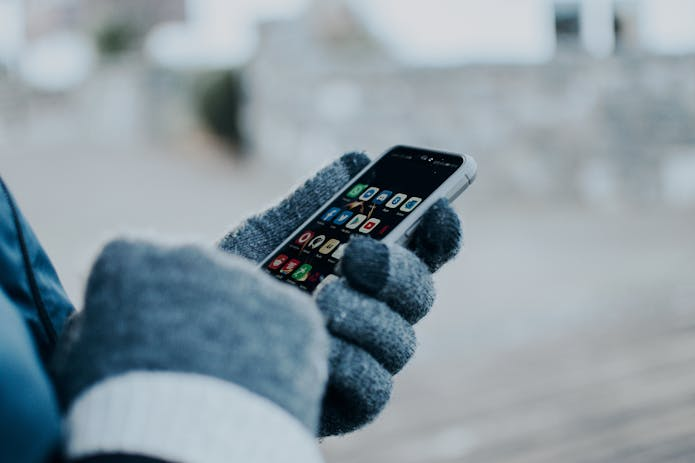 A person wearing gloves holding a cell phone, showcasing iOS 18.