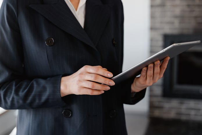  A professional woman in a suit confidently holds a New iPad Pro tablet, showcasing modern technology in a business setting.