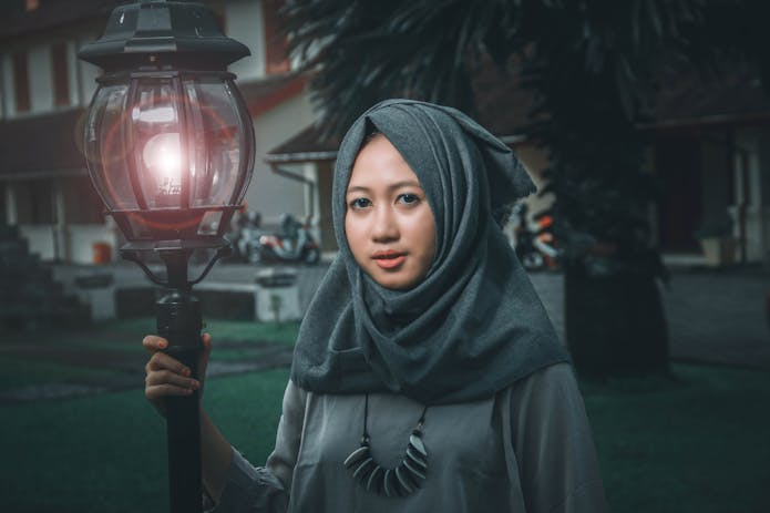 An elegant Muslim woman holding an LED lamp in darkness.