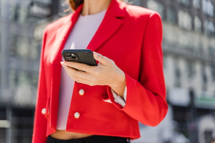 A woman in a striking red blazer is seen holding a cell phone, symbolizing the unveiling of iOS 18.