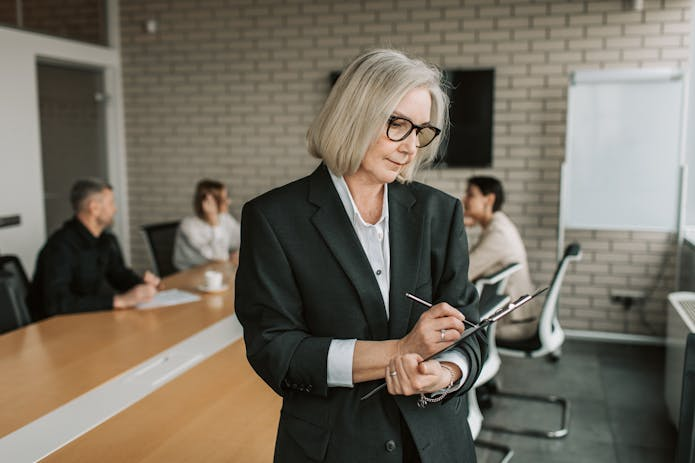 A woman in a business suit is focused on writing on a clipboard, reflecting the professionalism of a personal injury lawyer.